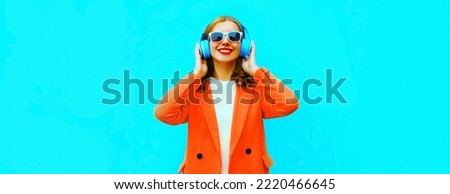 Portrait of happy smiling young woman in headphones listening to music wearing red jacket on blue background