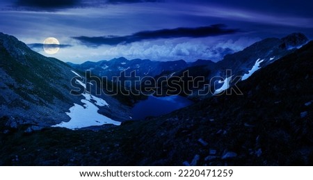 panoramic view of a lake in fagaras mountains at night. summer landscape on in full moon light. travel season in romania
