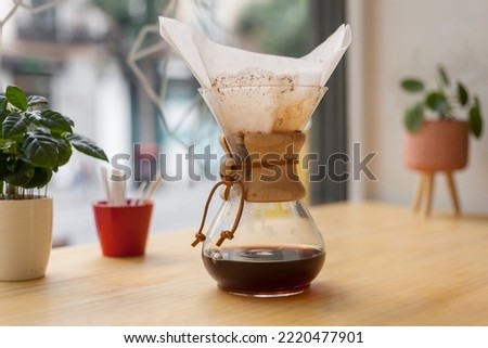 Chemex filter coffee elaboration concept with coffee liquid pouring inside the glass on a sunny coffee shop window. Royalty-Free Stock Photo #2220477901