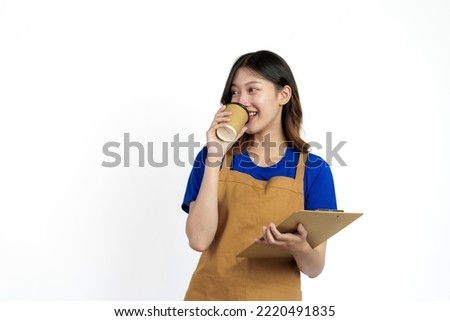 Cheerful young pretty asian woman blue t-shirt and apron coffee owner isolated on white background. Holding paper coffee up and clipboard