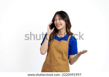 Cheerful young pretty asian woman blue t-shirt and apron coffee owner isolated on white background. call mobile phone, recieve order