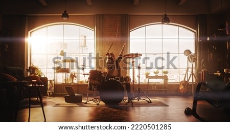 Young Female Playing Drums During a Band Rehearsal in a Loft Studio with Warm Sunlight at Daytime. Drummer Girl Practising Before a Live Concert on Stage. Talented Musician Enjoying Music. Royalty-Free Stock Photo #2220501285