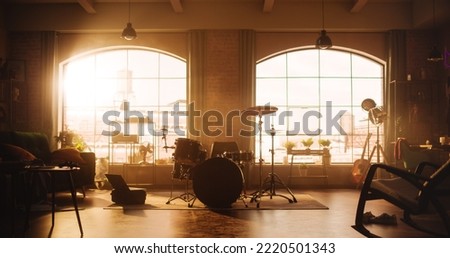 Establishing Shot: Music Rehearsal Studio in Loft Room with Drum Set in the Middle. Stylish Interior with Two Big Windows, Cozy Sofa, Shelves and Plants. Sunny Bright Day and Urban City View.