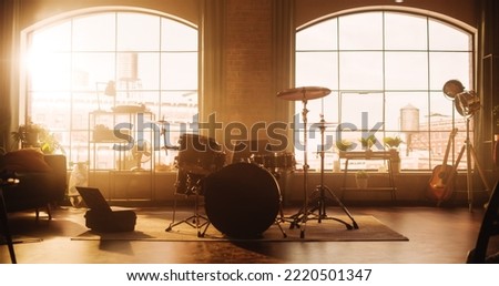 Establishing Shot: Music Rehearsal Studio in Loft Room with Drum Set in the Middle of It. Stylish Interior with Two Big Windows, Cozy Sofa, Shelves and Plants. Sunny Bright Day and Urban City View. Royalty-Free Stock Photo #2220501347