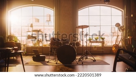 Establishing Shot: Music Rehearsal Studio in Loft Room with Drum Set in the Middle. Stylish Interior with Two Big Windows, Cozy Sofa, Shelves and Plants. Sunny Bright Day and Urban View.