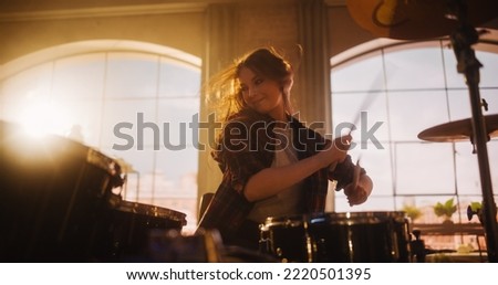 Portrait of a Young Female Playing Drums During a Band Rehearsal in a Loft Studio with Warm Sunlight at Daytime. Drummer Girl Practising Before a Live Concert on Stage in Local Venue. Royalty-Free Stock Photo #2220501395