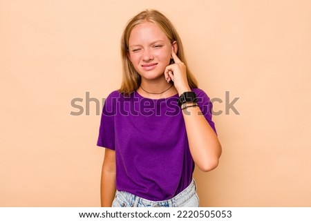 Caucasian teen girl isolated on beige background covering ears with hands. Royalty-Free Stock Photo #2220505053