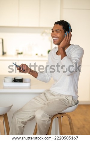 Young man sitting in the kitchen and listening to music in headphones