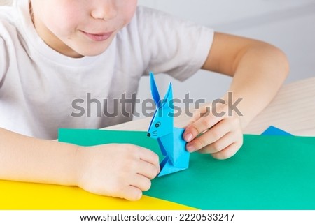 Children's craft origami blue rabbit. Origami blue paper rabbit in the hands of a child. Symbol of the year.