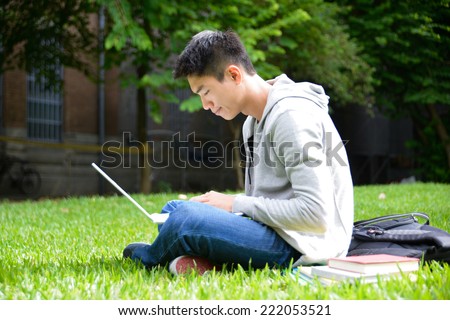 male college student use laptop on a grass at a campus 