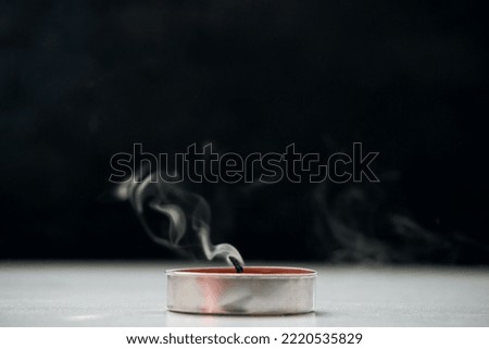 A extinguished candle emitting smoke standing on the table, a black background. Soft selective focus