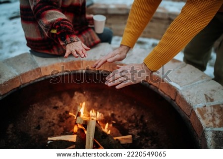 Senior couple sitting and heating together at outdoor fireplace in winter evening. Royalty-Free Stock Photo #2220549065
