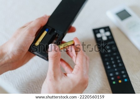 cropped shot of female hands insert new battery in tv remote control for watching television at home Royalty-Free Stock Photo #2220560159