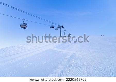 Ski chair lift on top of mountain, ski slope prepared for skiing, minimal style blue monochrome winter scene in  Sheregesh ski resort. White snow, clear sky, cable road and small people on peak Royalty-Free Stock Photo #2220563705