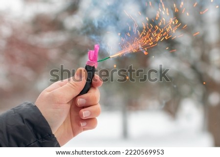Burning Firecracker in a Hand. Guy Holding a Petard Outdoors in Winter at Daytime. Loud and Dangerous New Year's Entertainment. Hooliganism with Pyrotechnics. Noise of Firecrackers in Public Places Royalty-Free Stock Photo #2220569953