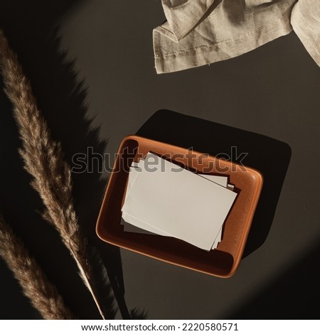 Flatlay of blank paper cards, plate, linen cloth, pampas grass, sunlight shadows on dark background. Business template. Top view, flat lay aesthetic luxury bohemian business branding concept