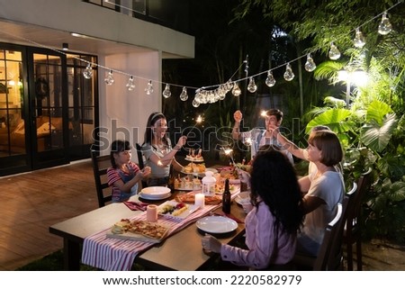 Party of friends and family outside sitting around a table with lights eating food and holding sparklers