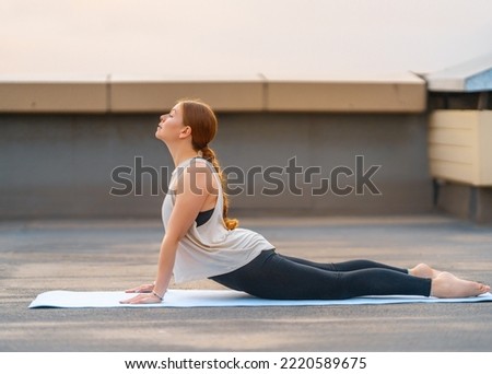 Young sportswoman is doing yoga exercise on rooftop of parking, garage in summer day morning.