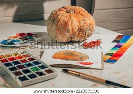 Drawing in watercolor in a sketchbook. Autumn still life with pumpkin and red leaf. Learning to draw at home. Creating content concept.