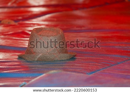 Fabric hat, solitary, on top of blue mats, with red reflection. Focus on a specific point on the hat.