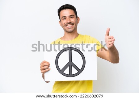 Young handsome man over isolated white background holding a placard with peace symbol making a deal