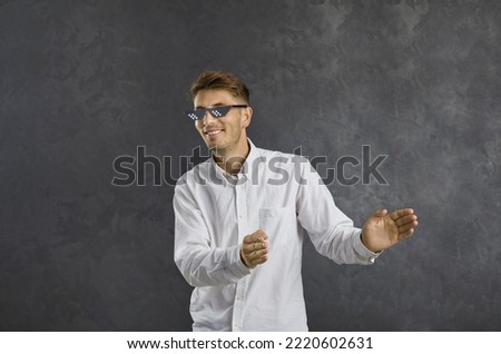 Portrait of funny positive young man in modern thug life sunglasses enjoying music and having fun. Happy cheerful guy in pixel glasses dancing isolated on grey background