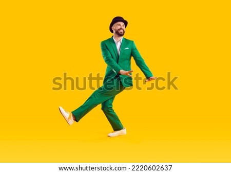 Specifics of Irish culture. Cheerful man in green modern suit and hat is dancing and having fun celebrating St. Patrick's Day. Full length festive young man on orange background. Idea for banner.