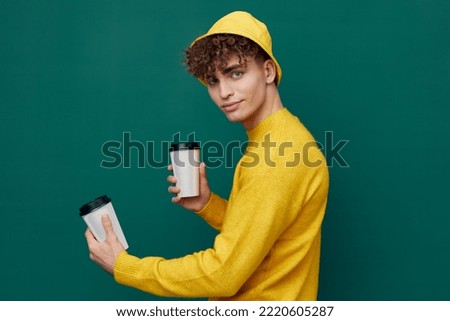 a joyful man stands on a green background in bright clothes and holds two coffee glasses in his hands, smiling affably at the camera