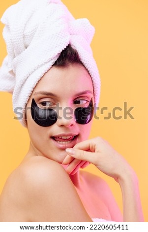 Horizontal photo, a woman with perfect skin on an orange background in a towel on her head and body with black patches on her face and even teeth gently smiles