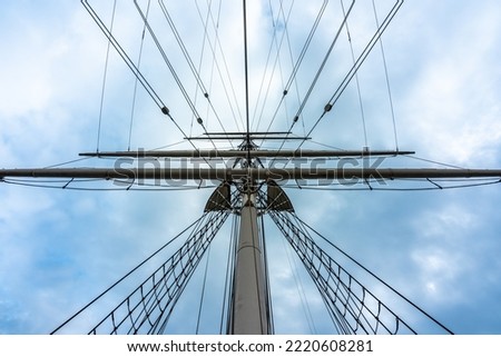 Vertical perspective view of a tall mast spar with ropes and boms on a tall ship with blue sky.