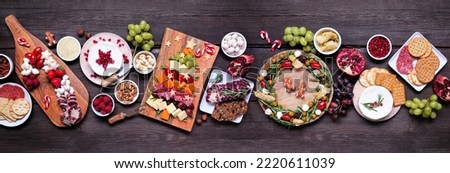 Christmas charcuterie table scene against a dark wood banner background. Assorted cheese and meat appetizers. Christmas tree, wreath and candy cane arrangements.
