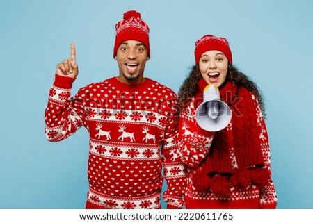 Merry young couple two man woman wear red Christmas sweater Santa hat posing hold scream megaphone announces sale point finger up isolated on plain pastel blue background Happy New Year 2023 concept Royalty-Free Stock Photo #2220611765