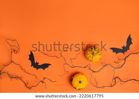 Two small decorative pumpkins, black paper bats, bare branches on bright orange background. Happy Halloween composition. Fall seasonal sale template. Copy space for text, top view, flat lay.