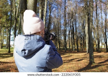 Photographer woman with DSLR camera and zoom lens take photos in autumn Park on yellow fall leaves