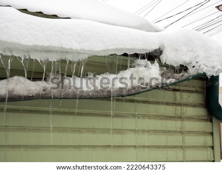 Gutter broken by snow masses sliding from the roof Royalty-Free Stock Photo #2220643375