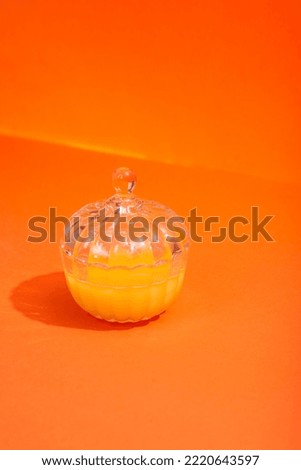 Orange jam in a glass jar on an orange background