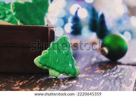 Frosted Christmas tree shape cookies or biscuits with green icing on a rustic table. Selective focus with blurred foreground and background.