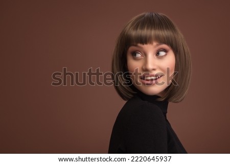 Portrait of a beautiful smiling brunette girl with a short haircut. Brown background. Royalty-Free Stock Photo #2220645937
