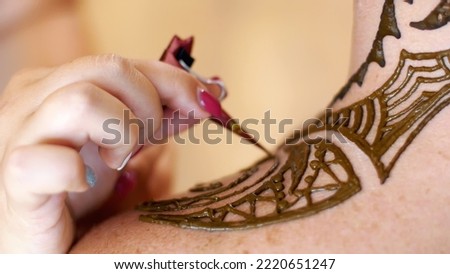 A close-up of the drawing, ornament, henna tattoo, on the scalp, shoulder, neck. The solution of henna dries on the skin. The process of applying henna from a tube to the skin. High quality photo
