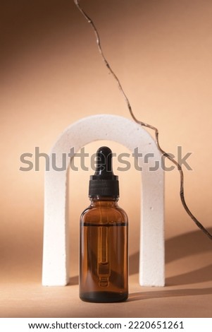 Glass dropper bottle with cosmetic oil stand in arch on a pastel background with branch tree. Herbal homeopathic products. Natural organic spa cosmetics.
