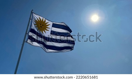 Uruguay flag waving on clear blue sky with sun
