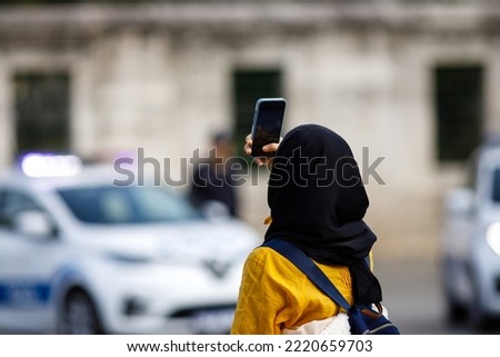 Young Islamic woman taking photos on phone, back view. Shooting video with cell phone camera, using smartphone to take pictures outdoor. Tourist photographing landscape. 
