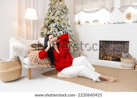 A picture of a young, positive woman in a Christmas atmosphere talking on the phone and smiling. Talking on the phone at Christmas