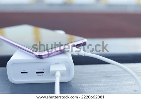 phone is charged from the power bank, portable charger on the bench Royalty-Free Stock Photo #2220662081