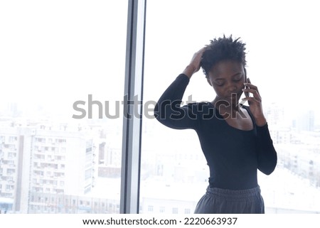 A young African-American woman in sportswear using phone and looks down. A young woman touches her short haircut. Lifestyle photo with copy space. High quality photo