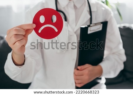 Woman doctor in white uniform with stethoscope holding little red angry emoticon and clipboard. Emotional intelligence, balance emotion control, mental health assessment, bipolar disorder concept Royalty-Free Stock Photo #2220668323