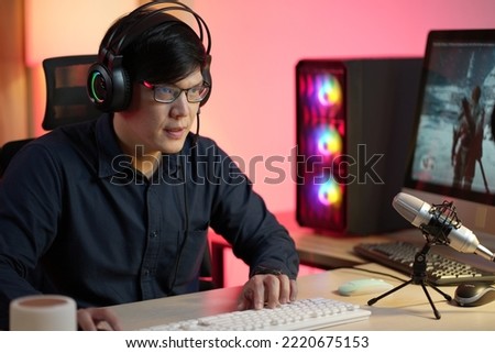 Professional Gamer Playing First-Person Shooter Online Video Game on His Powerful Personal Computer. Room and PC have Colorful Neon Led Lights. Young Man Cozy Evening at Home.
