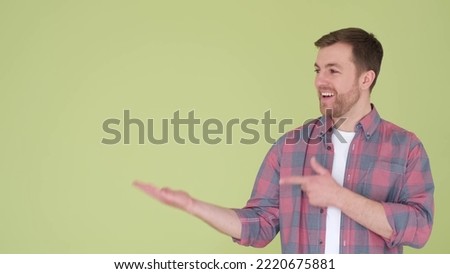 Caucasian man pointing finger at copy space isolated on yellow and green background. A young handsome man demonstrates an idea or advertises something
