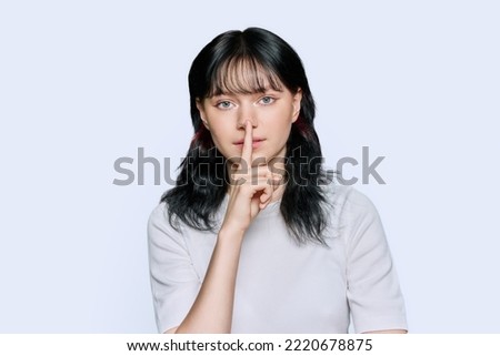 Young woman showing silent gesture with finger on lips, white background