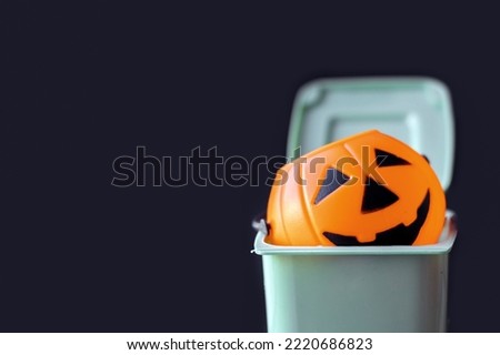 pumpkin halloween plastic spooky smiling pumpkin in mini small trash bin can.holiday it's over concept or denied not accepted.trash bin isolated on black background.trick or treat holiday scary 